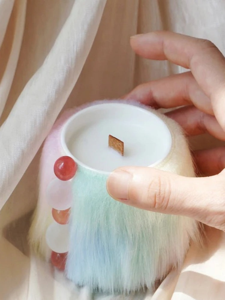 Hand holding a small, round, pastel-colored product with a fluffy texture against a soft background.